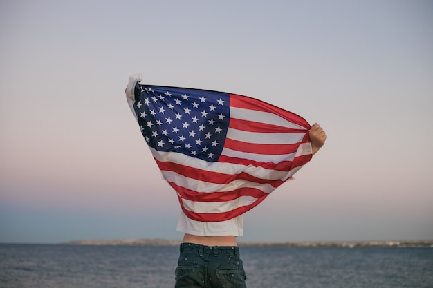 Le petit garçon laisse le drapeau américain flotter dans ses mains sur le vent à la mer