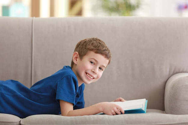 Petit garçon lisant un livre sur un canapé à l'intérieur