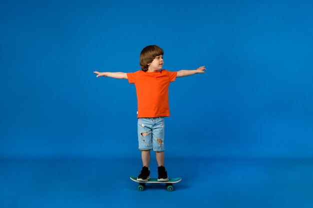 Petit Garçon Ludique Aux Cheveux Bruns Monte Une Planche à Roulettes Sur Une Surface Bleue Avec Une Place Pour Le Texte