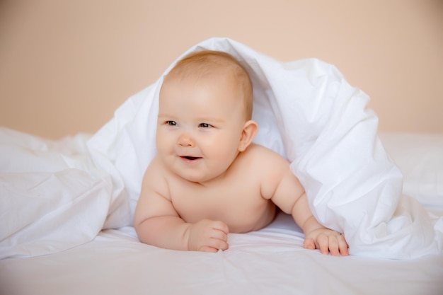 petit garçon à la maison dans la chambre allongé sur un drap blanc enveloppé dans une serviette après le bain