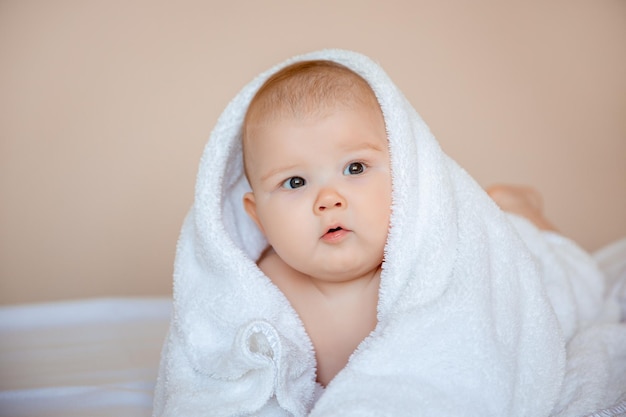 petit garçon à la maison dans la chambre allongé sur un drap blanc enveloppé dans une serviette après le bain