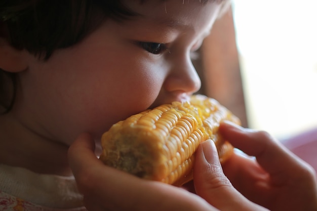 petit garçon mange avidement le grain de maïs mordant