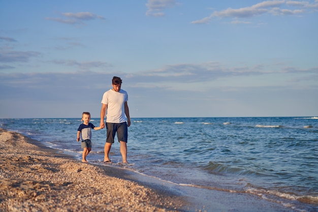 Petit garçon marchant avec le père à la plage. Été