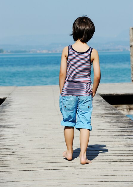 Petit garçon marchant sur le quai par la belle mer