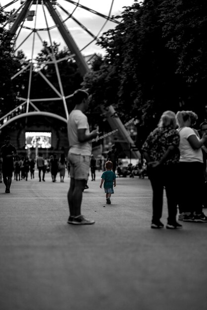 Un petit garçon marche parmi la foule de gens dans le parc Photo en noir et blanc