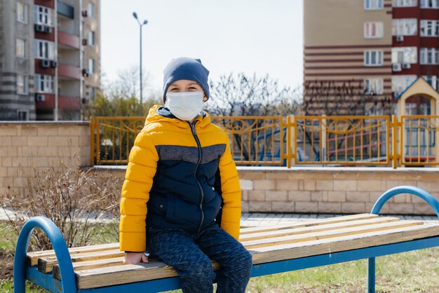 Un petit garçon masqué marche sur l'aire de jeux pendant la quarantaine. Reste à la maison