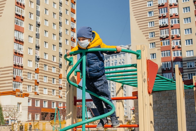 Un petit garçon masqué marche sur l'aire de jeux pendant la quarantaine. Reste à la maison.