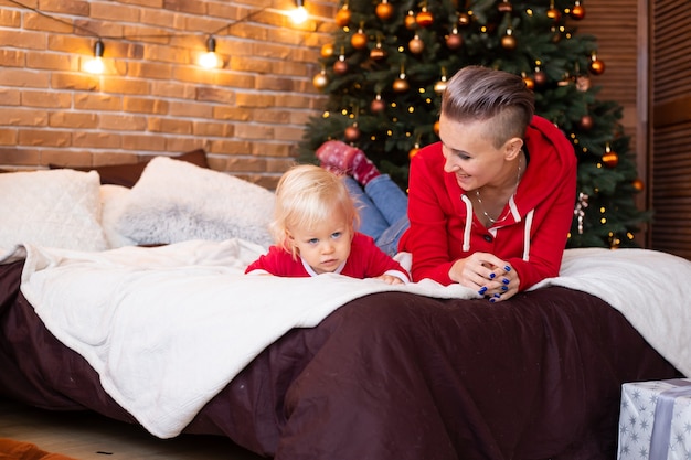 Petit garçon et mère mignons sur le lit dans la salle décorée de fête pour Noël