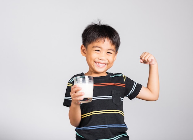 Petit garçon mignon de 5 ans souriant tenant un verre de lait et montrant un geste fort de puissance