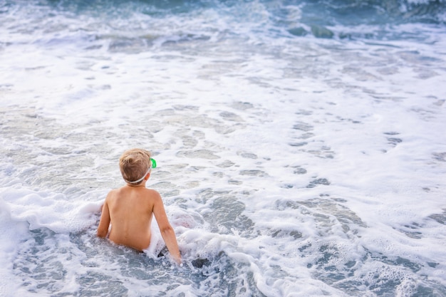 Petit garçon mignon bébé caucasien aux cheveux blonds joue à la plage dans les vagues de la mer le jour de l'été ensoleillé.