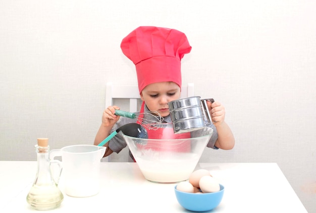 Un petit garçon mignon dans une toque rouge pétrit la pâte à pâtisserie dans un bol. Gâteaux faits maison.
