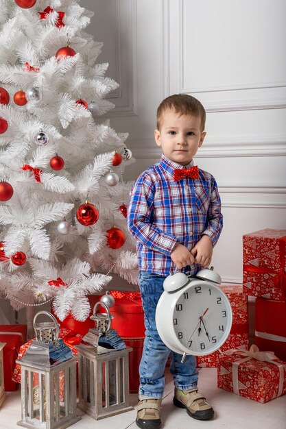 Petit garçon mignon décontracté habillé debout dans une salle blanche parmi les décorations de noël