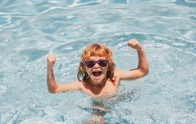 Petit garçon mignon excité dans des lunettes de soleil dans la piscine en journée ensoleillée, l'enfant se détend dans la piscine d'été