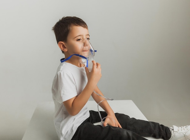 Le petit garçon mignon fait l'inhalation. L'enfant tient un inhalateur à la main et est traité pour une toux. photo de studio de haute qualité.