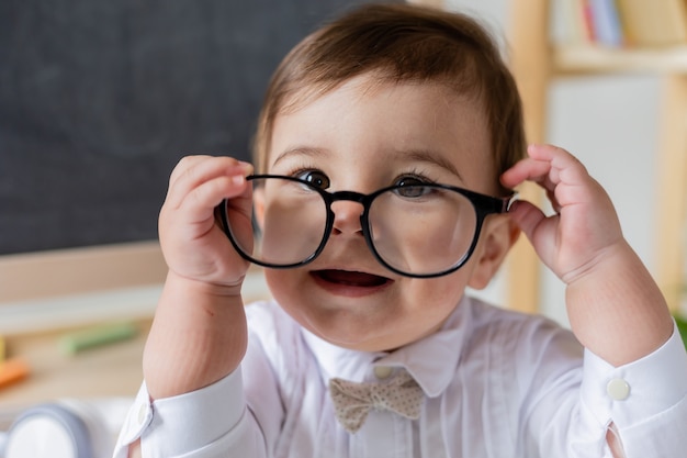 Un petit garçon mignon avec des lunettes souriant à côté du tableau noir et des livres. éducation préscolaire pour les enfants