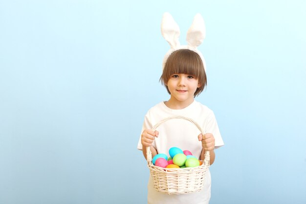 Petit garçon mignon avec des oeufs de pâques dans ses mains et des oreilles de lapin sur la tête