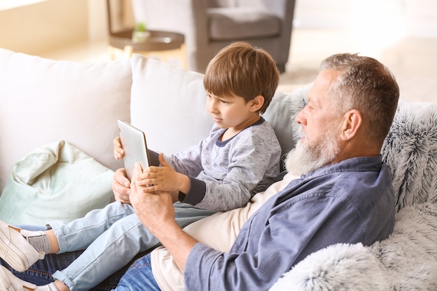 Petit garçon mignon et son grand-père avec tablette à la maison