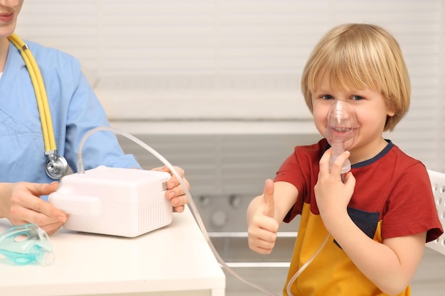Photo un petit garçon montre les pouces en l'air en utilisant un nébuliseur pour l'inhalation à l'hôpital