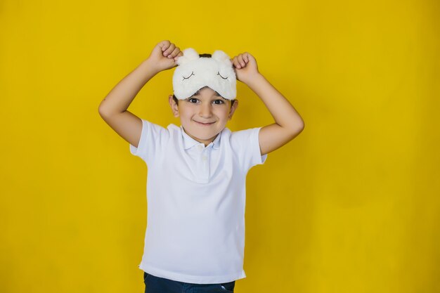 Un petit garçon sur un mur jaune vif dans un masque de sommeil accessoire à la mode.