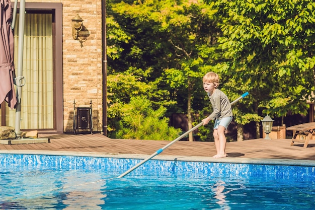 Le petit garçon nettoie la piscine et sort la balle de la piscine concept de nettoyeur de piscine