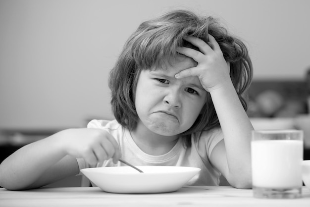 Petit garçon non focalisé ayant de la soupe pour le déjeuner malheureux enfant caucasien assis à table à la cuisine à la maison