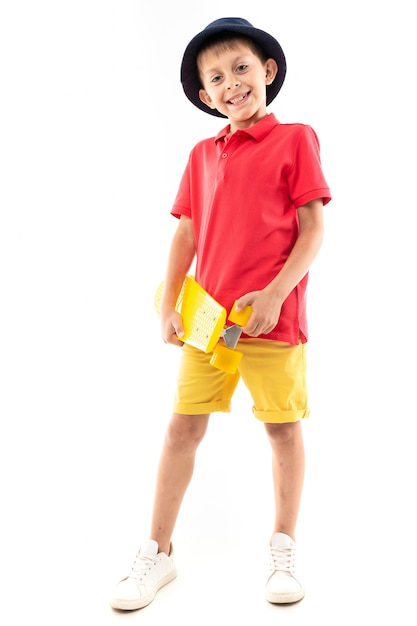 Un petit garçon en panama, en jersey jaune, short rouge et baskets blanches se tient et tient un sou jaune dans ses mains