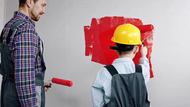 Un petit garçon peignant des murs avec de la peinture rouge son père le regardant