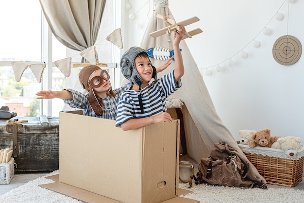 Petit garçon et petite fille dans des chapeaux de pilote jouant des pilotes assis dans une boîte en papier à la maison