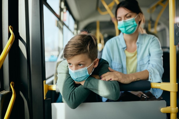 Petit garçon portant un masque facial tout en faisant la navette avec sa mère en bus