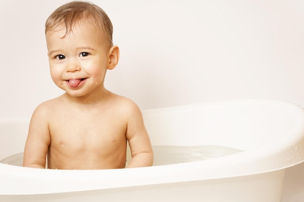 Le petit garçon prenant un bain colle une langue dans l'eau chaude