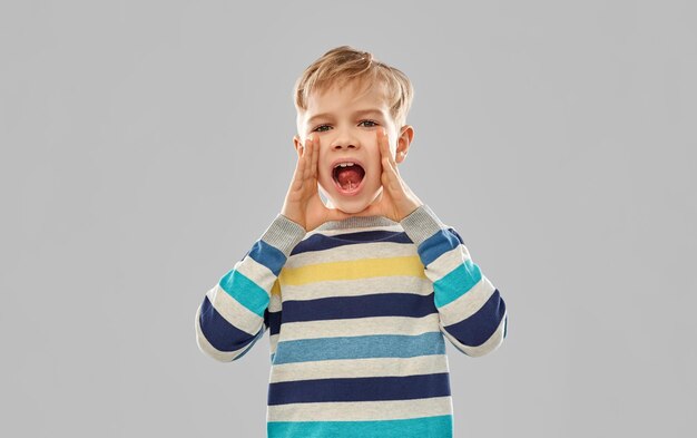 Un petit garçon en pull rayé qui appelle quelqu'un.