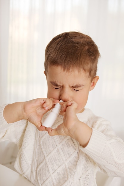 Petit garçon pulvérisant des médicaments dans le nez, gouttes nasales. Enfant en bas âge utilisant un spray nasal. Nez qui coule, rhume, grippe, maladie, virus. Fermer.