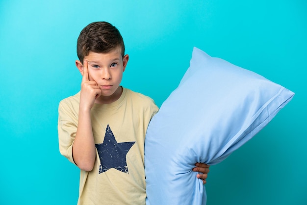 Petit garçon en pyjama isolé sur fond bleu pensant à une idée