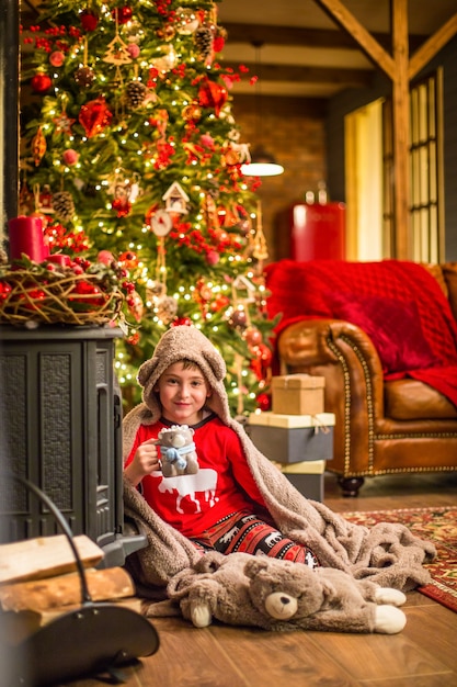 Un petit garçon en pyjama de Noël est assis près d'un arbre de Noël