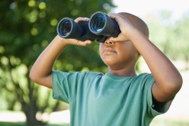 Photo petit garçon regardant à travers des jumelles dans le parc