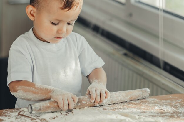 Un petit garçon avec un rouleau à pâtisserie dans la cuisine préparant la cuisson de la pâte