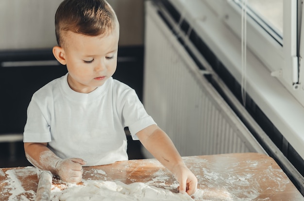 Un petit garçon avec un rouleau à pâtisserie dans la cuisine préparant la cuisson de la pâte