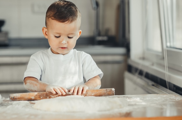 Un petit garçon avec un rouleau à pâtisserie dans la cuisine préparant la cuisson de la pâte