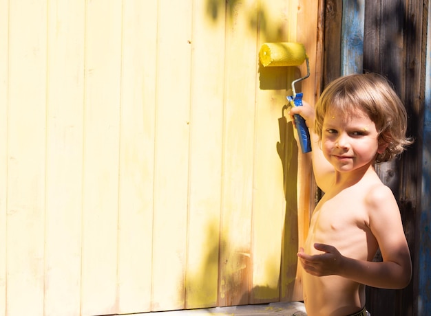 Un petit garçon avec un rouleau peint la maison avec de la peinture jaune