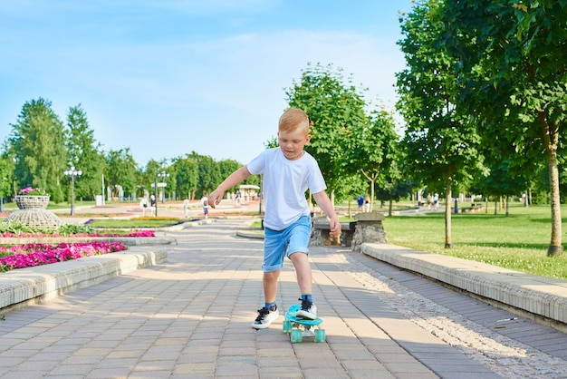 Un petit garçon roux apprend à patiner dans le parc en été