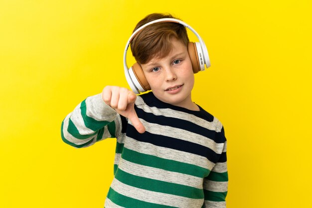 Petit garçon roux isolé sur fond jaune, écouter de la musique