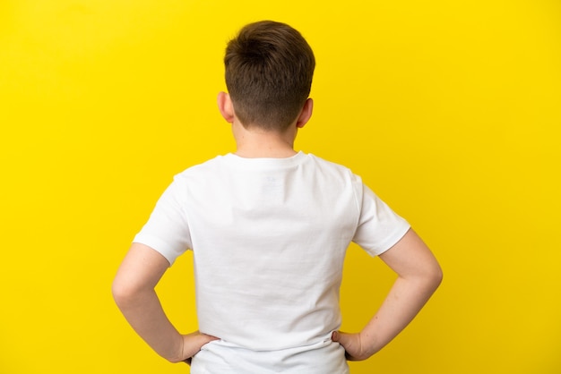 Petit garçon roux isolé sur fond jaune en position arrière