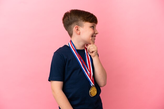 Petit garçon roux avec des médailles isolées sur un mur rose à côté