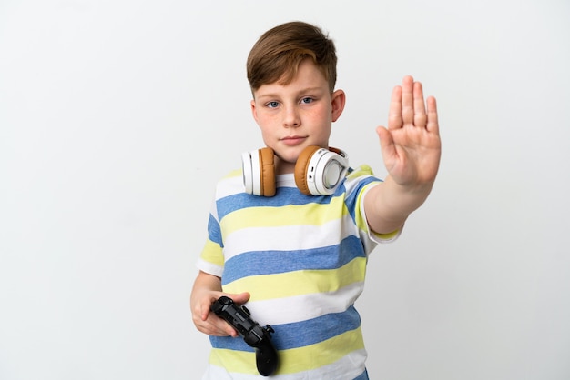 Petit garçon roux tenant une manette de jeu isolé sur fond blanc faisant un geste d'arrêt