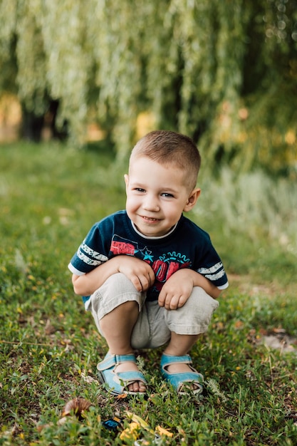 Le petit garçon s'assied dans l'herbe et sourit gentiment