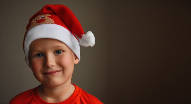 Petit garçon de santa dans le chapeau de Santa rouge sur un fond marron Bannière de Noël de portrait avec l'enfant