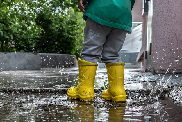 Petit garçon saute dans une flaque d'eau en bottes de caoutchouc par temps de pluie