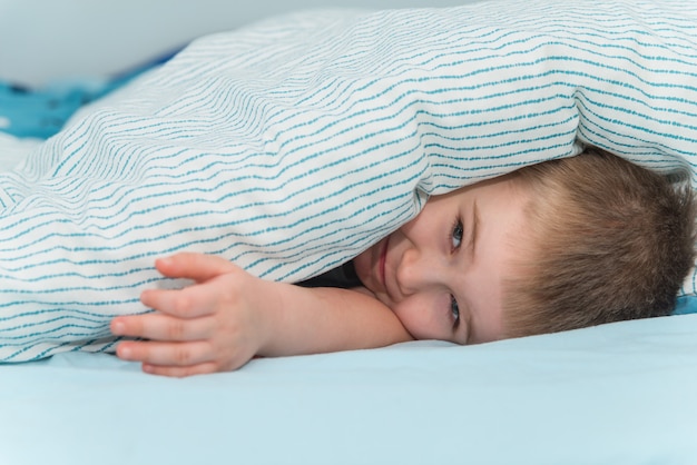 Petit garçon se couche sous la couverture et souriant