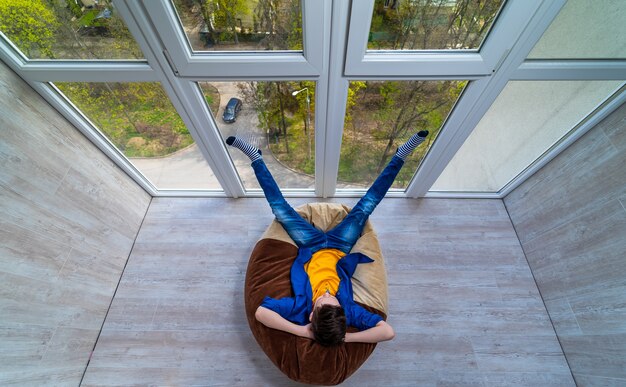 Petit garçon se détendre sur une terrasse. Adolescent rêvant de vocation estivale regardant à travers le mur de verre. Faire la sieste dans un fauteuil moelleux.