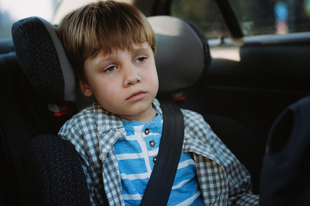 Petit garçon se sentant malade voyageant en voiture assis dans un siège enfant attaché avec ceinture